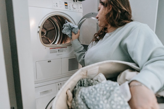 Person holding a laundry basket and loading laundry into a washing machine